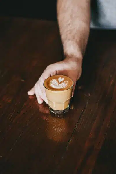 A barista holding a flat white in a glass