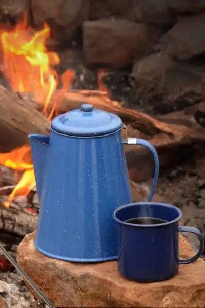 A percolator pot sitting by a fire