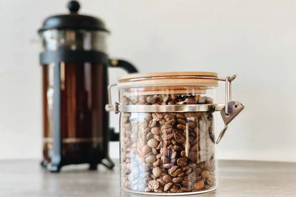 a jar of coffee beans in front of a french press