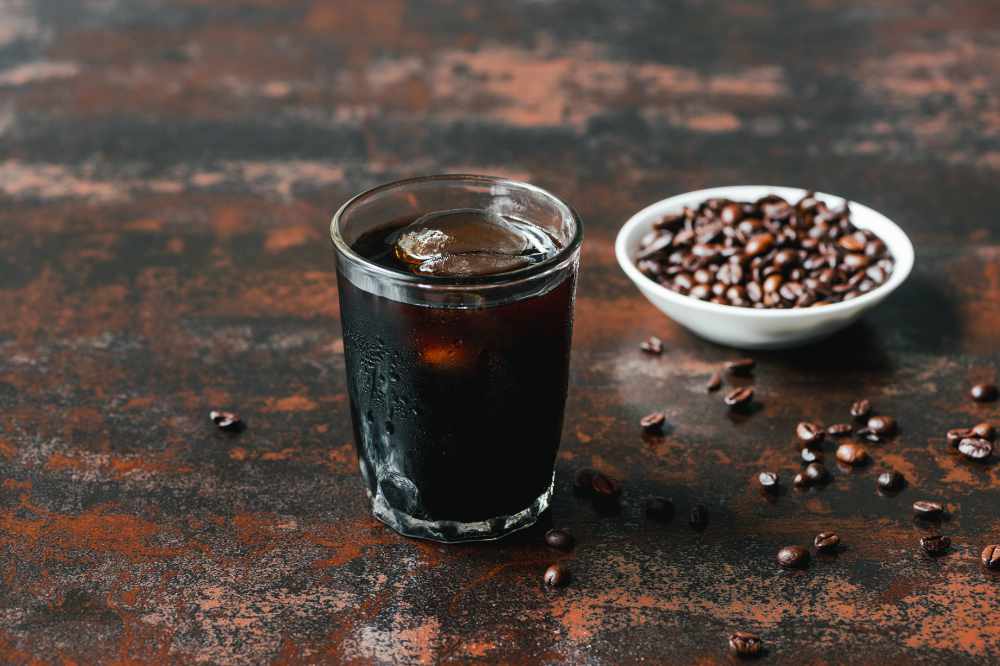 A cold brew coffee beside some coffee beans
