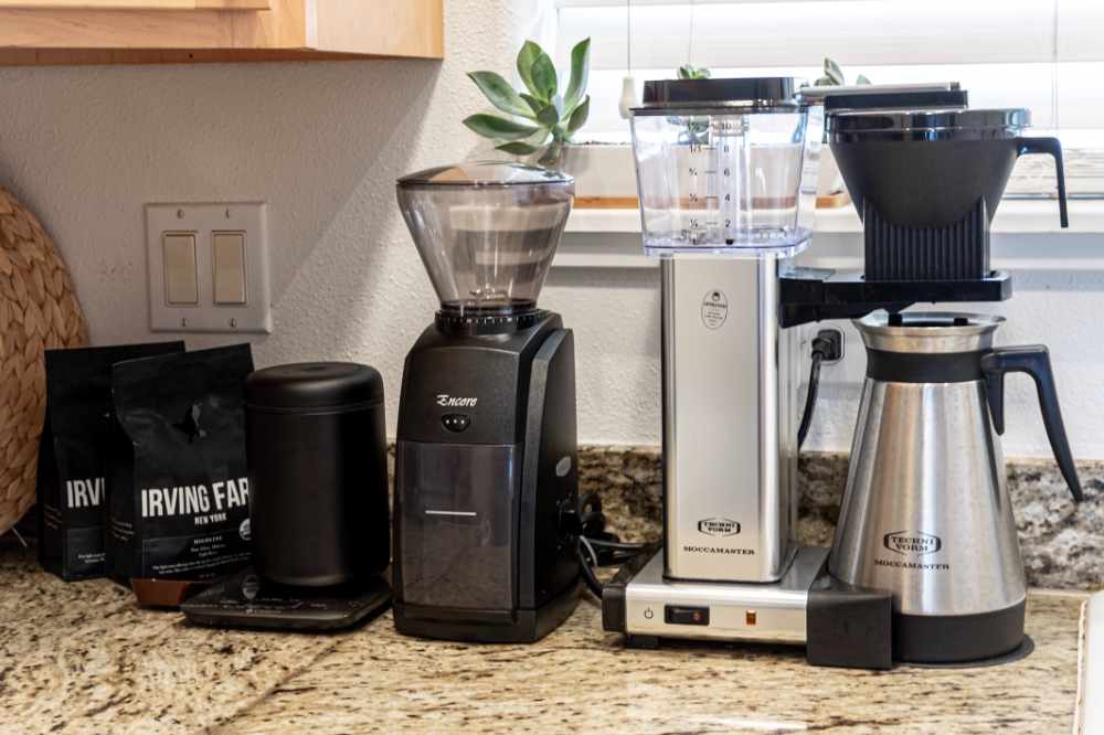a drip coffee machine beside a grinder and bags of beans