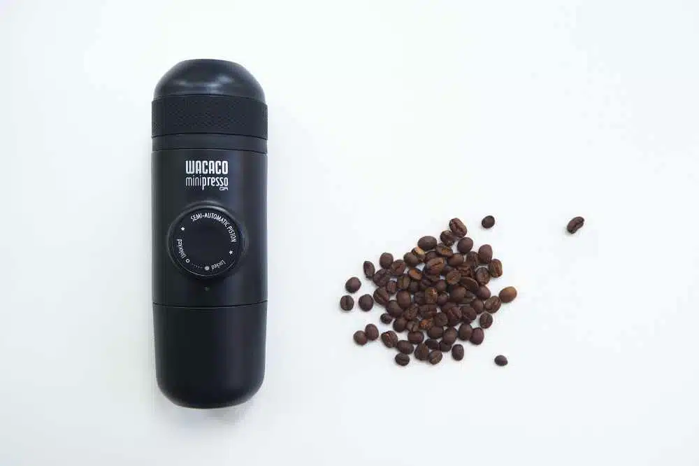 A Wacaco Minipresso GR lying next to some coffee beans