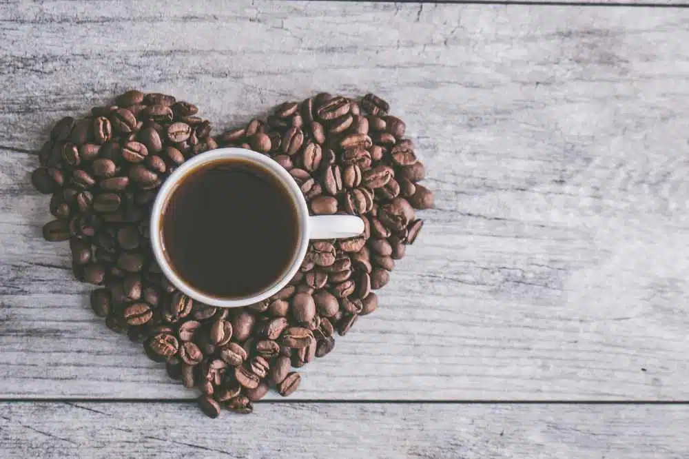 A cup of coffee surrounded by coffee beans in a love heart shape