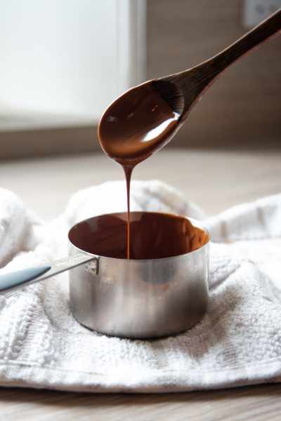 melted chocolate dripping off a wooden spoon into a pan