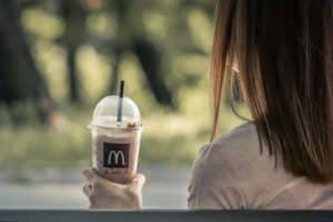 A girl sitting on a bench holding a mcdonalds iced coffee